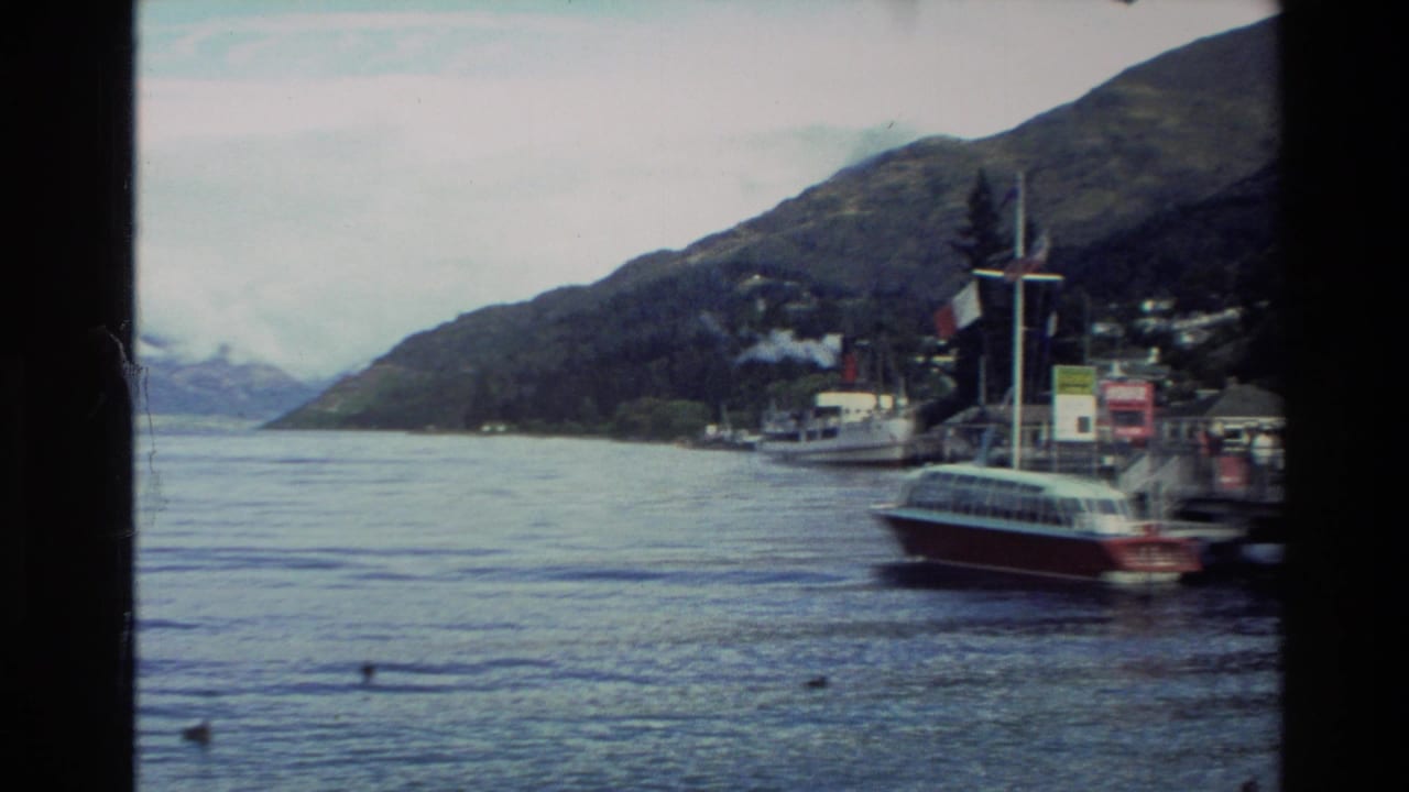 Small lakeside harbor with boats below steep mountains and cloudy sky.