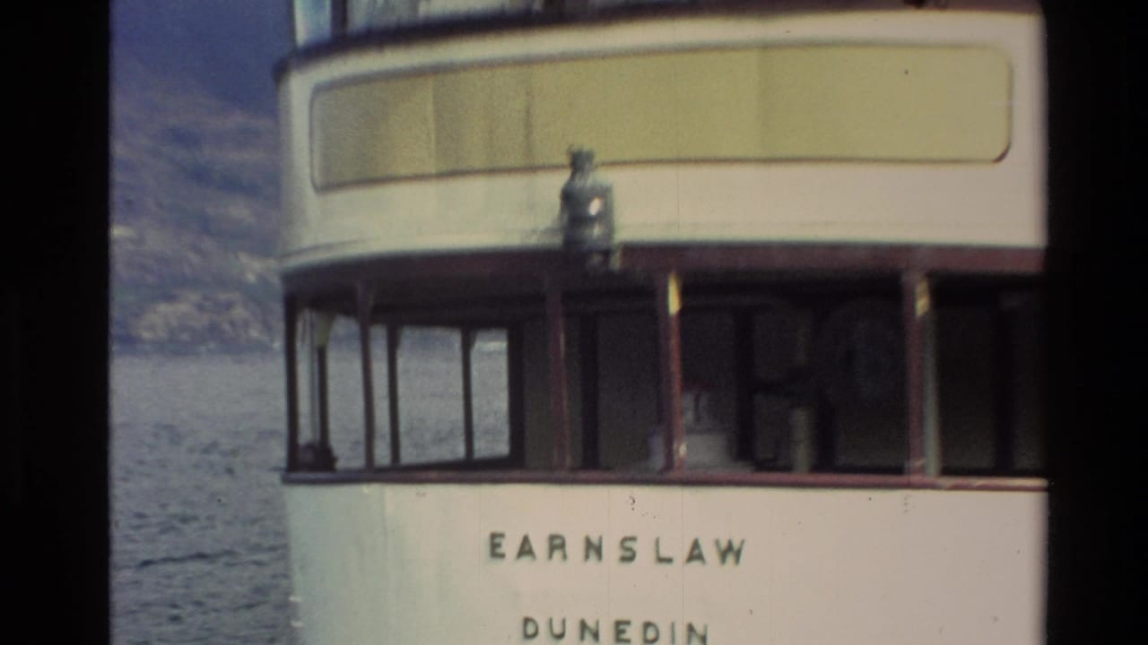 Close 1982 New Zealand 8mm view of the vessel stern, with Earnslaw and Dunedin lettering, windows, lake water, and a mountain backdrop.