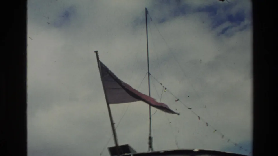 1982 New Zealand 8mm frame showing a flag and mast above the steamer, with rigging lines silhouetted against a cloudy sky.