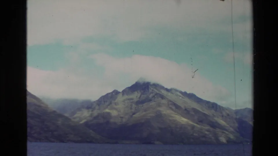 Scenic 1982 New Zealand 8mm frame of a rugged mountain across a lake, with no people visible in this still.