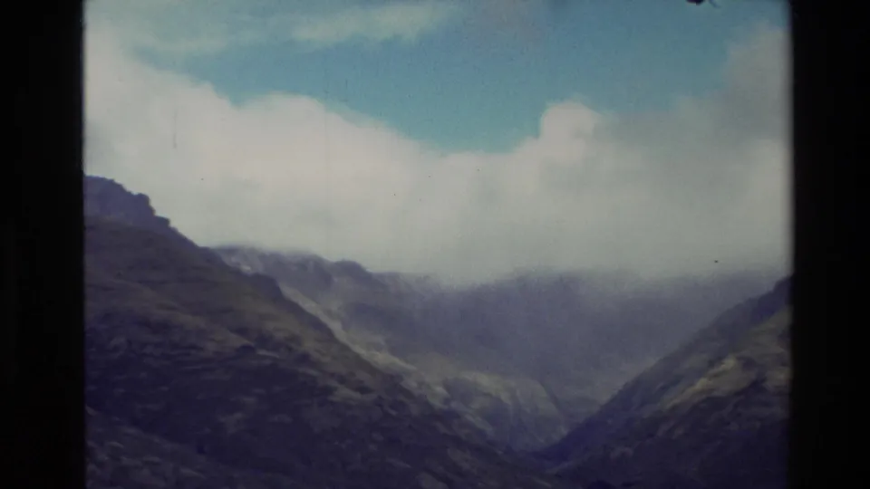 1982 New Zealand 8mm frame showing a deep green valley with clouds obscuring the upper mountain ridges.