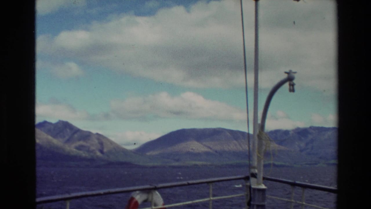 1982 New Zealand home-movie view from a boat deck, with railing and a curved lamp framing mountains beyond the water.