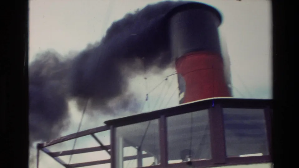 Close deck view of a red-and-black vessel funnel releasing dark smoke, with railings and rigging visible in the frame.