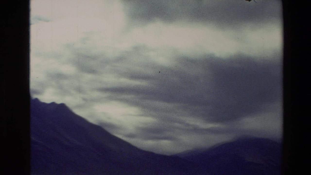 1982 New Zealand 8mm frame showing dark mountains under layered storm clouds, with muted blue-gray tones and film softness.
