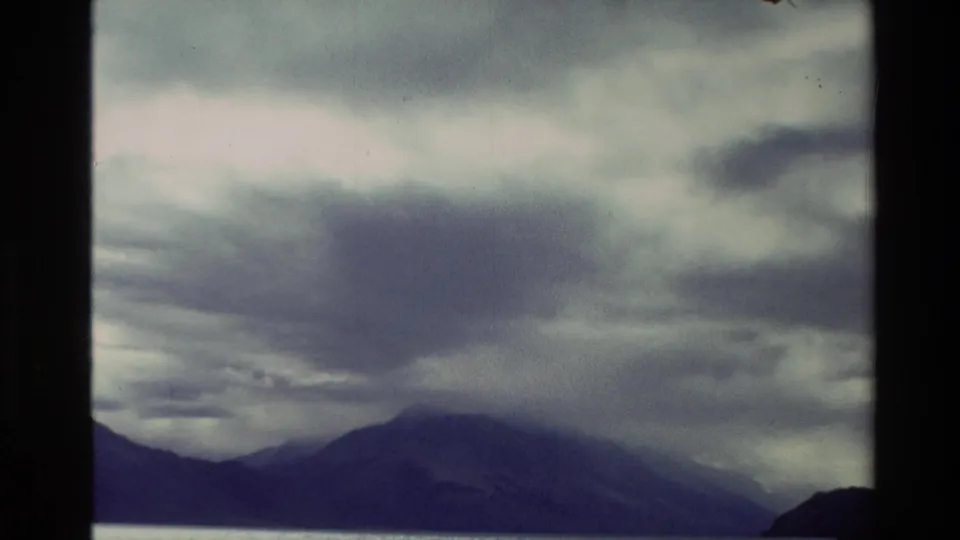 Vintage 8mm view from New Zealand showing a brooding cloud bank above distant mountains and a still water surface.