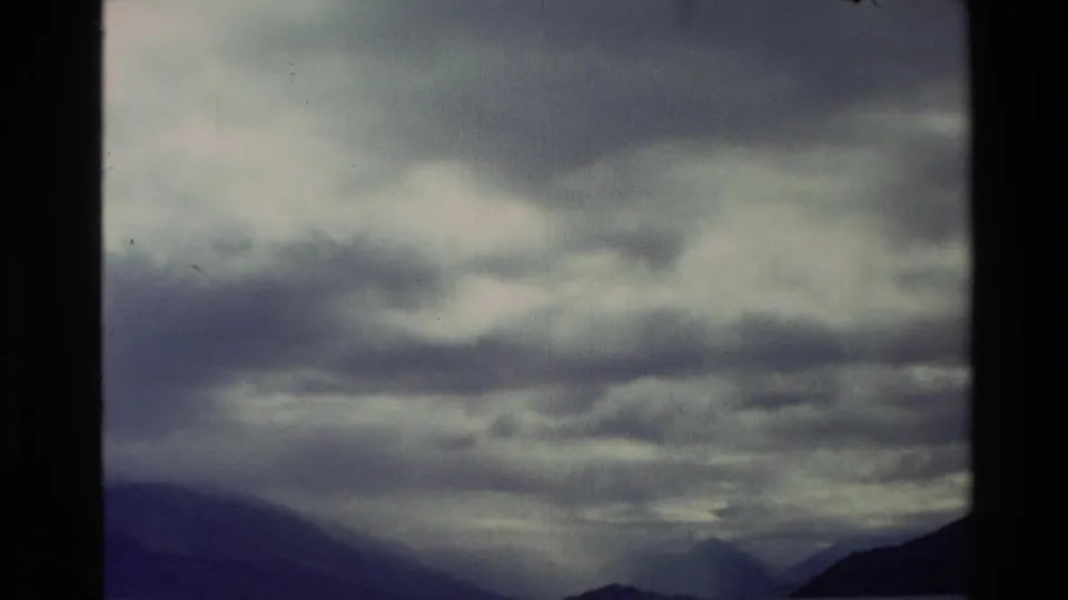1982 New Zealand 8mm frame showing heavy cloud over dark mountain ridges and a subdued valley horizon.