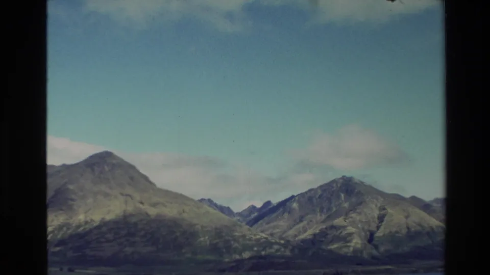 1982 New Zealand 8mm frame with clearer blue sky revealing rugged mountain peaks and sloping hills.