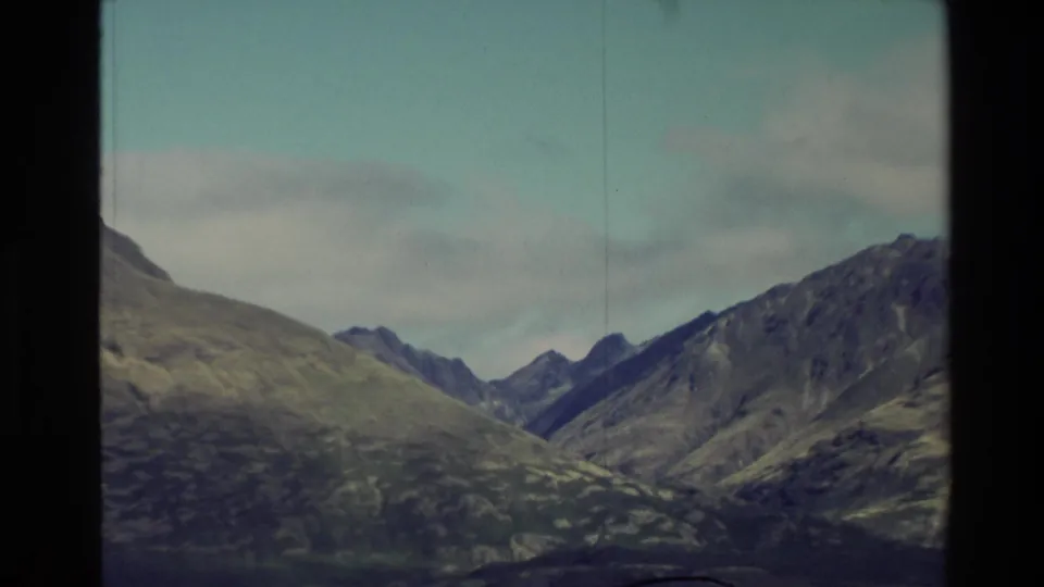 1982 New Zealand 8mm frame showing grassy mountain slopes and jagged ridges beneath a pale, clouded sky.