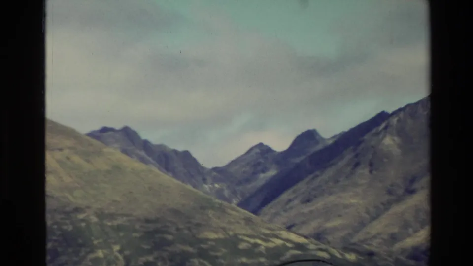 1982 New Zealand 8mm frame with layered mountain ridges, valley shapes, and cloud-softened light.