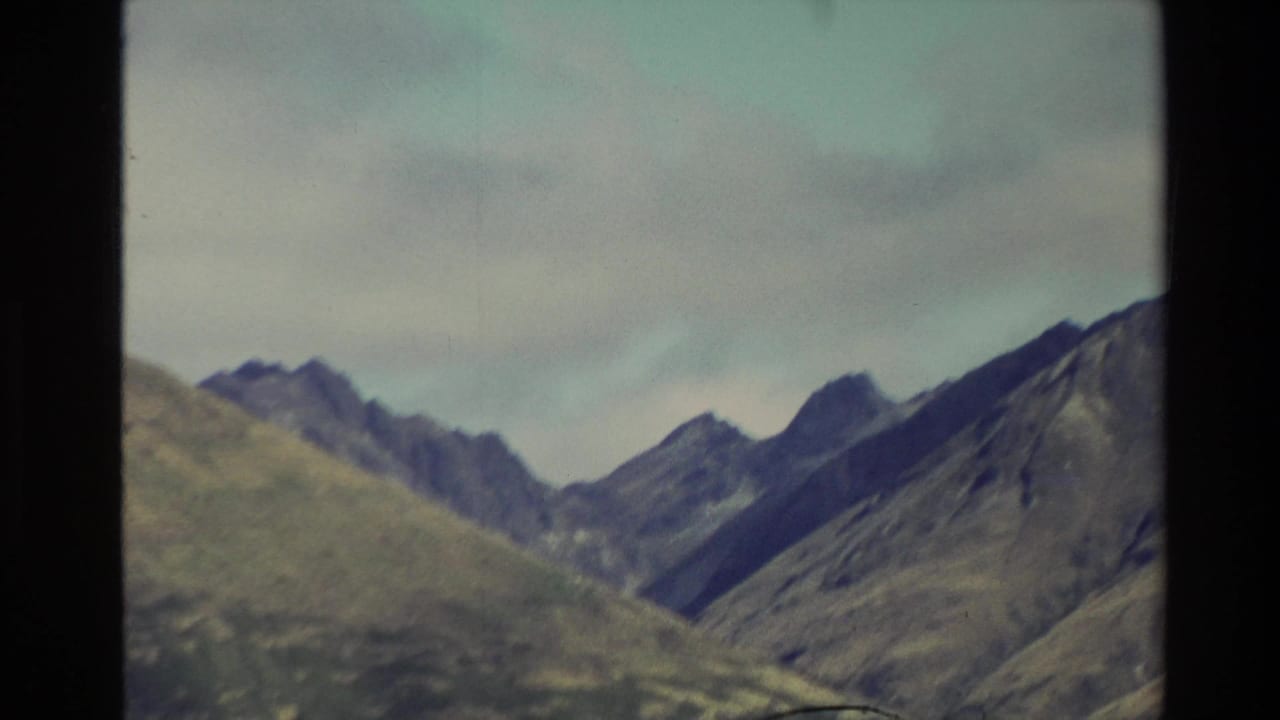 1982 New Zealand 8mm frame showing rugged mountain slopes and ridgelines through a dark window frame during travel.