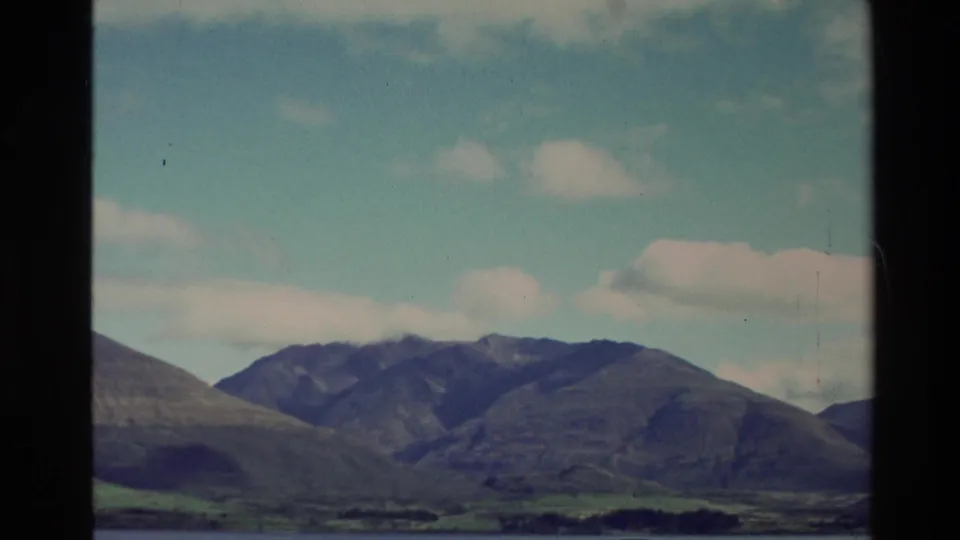 1982 New Zealand 8mm view of mountains and a lake, partially framed by a dark vehicle window.