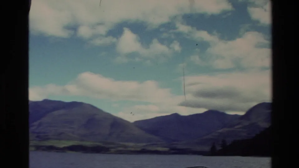 New Zealand mountain lakeshore under a partly cloudy sky, seen through dark window framing on 8mm film.