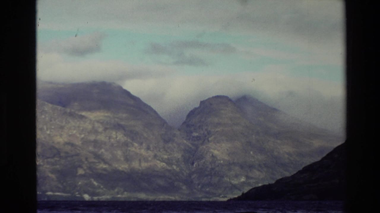 Misty mountain slopes across water or dark foreground under a partly cloudy sky.