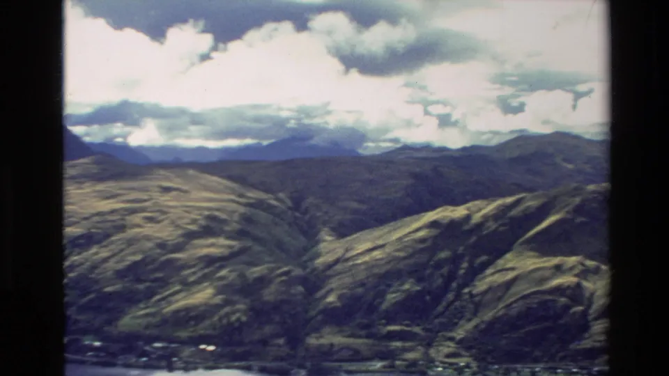 1982 New Zealand 8mm aerial view of broad mountain ridges, distant peaks, and broken white cloud above the valley.