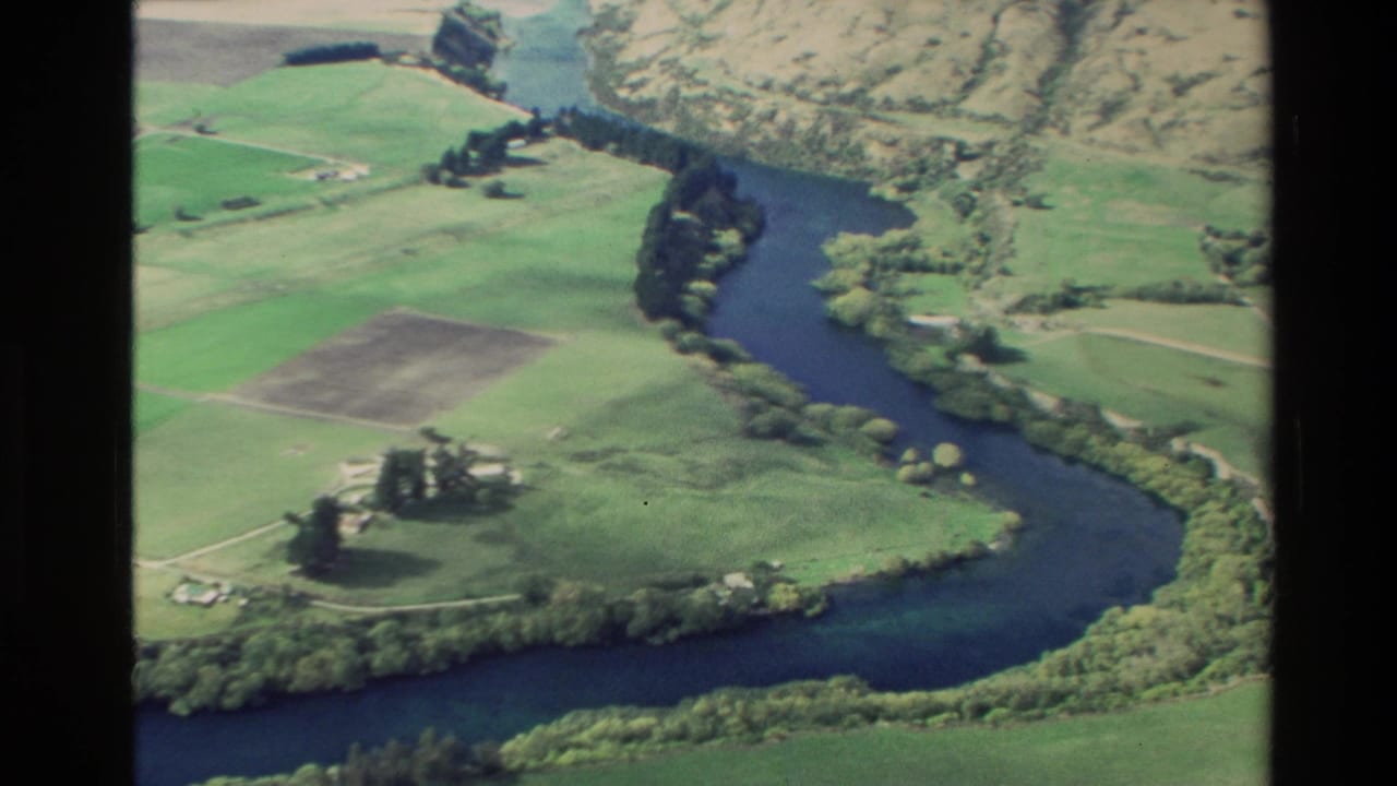 Aerial view of a river bend through farmland with hills beyond.