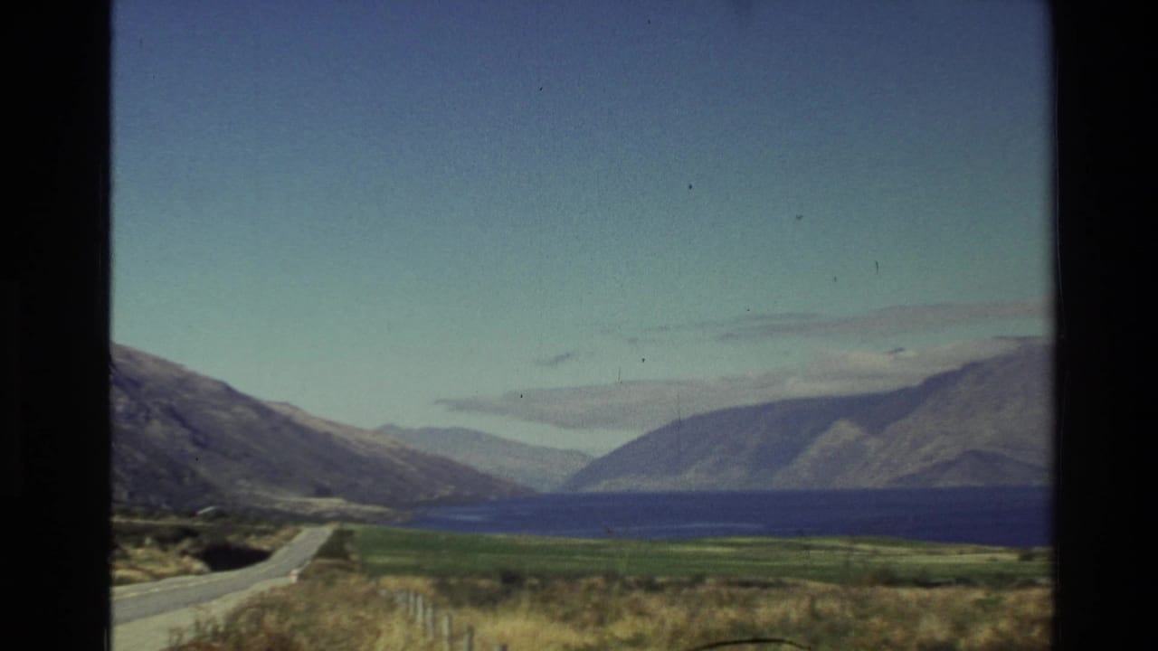 Winding road beside a lake with mountains rising beyond the shoreline.