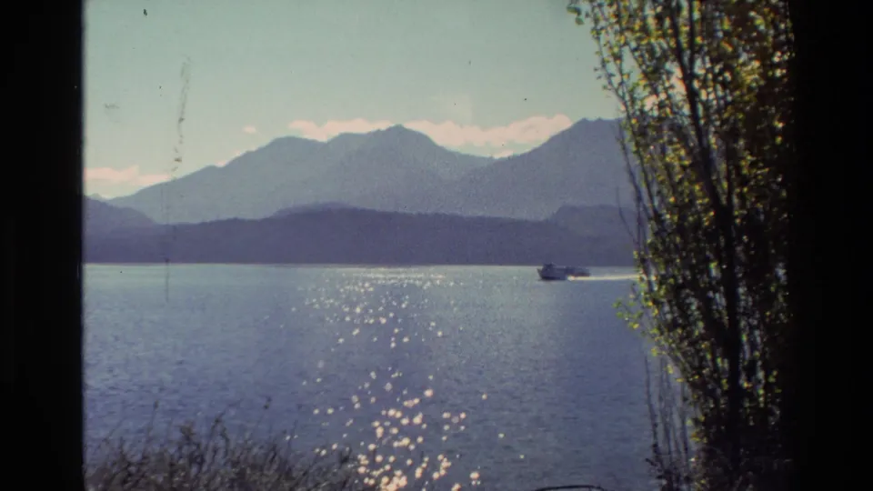1982 New Zealand 8mm frame with a small boat on sparkling lake water, backed by mountains and trees along the shore.