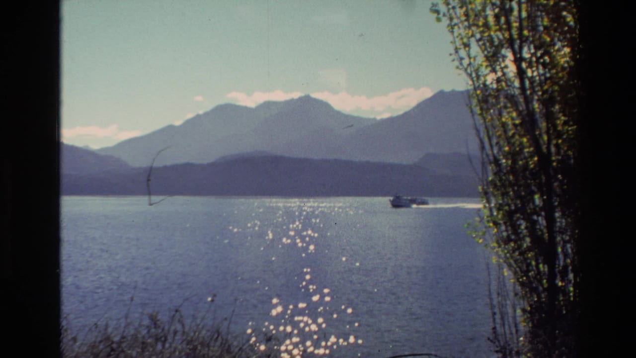 Small motorboat crosses a calm lake with mountains and sunlit water in the distance.