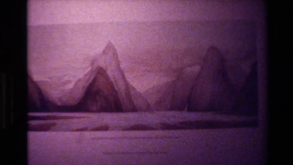 1982 New Zealand 8mm still of static mountain artwork, showing peaked forms, pale foreground, grain, soft projection, and magenta color fading.