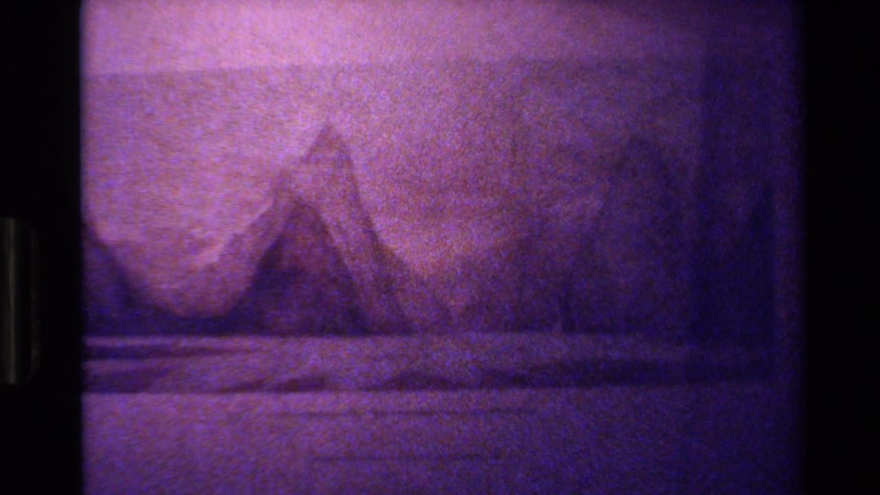 1982 New Zealand home-movie frame showing a purple-tinted topographic map with mountain shading and soft 8mm grain.
