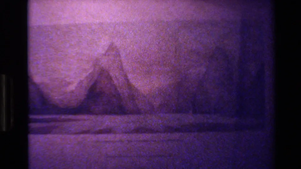 1982 New Zealand home-movie frame showing a purple-tinted topographic map with mountain shading and soft 8mm grain.