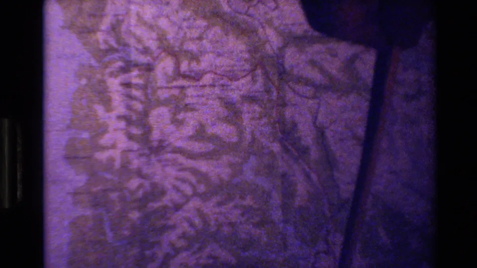 A close 8mm frame of a New Zealand topographic map, tinted purple, with terrain markings and a dark film edge.