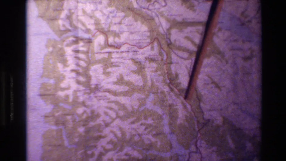 A narrow pointer traces near a red line on a purple-tinted New Zealand map in grainy 8mm footage.