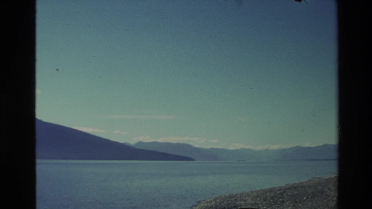 1982 New Zealand home-movie view of a calm lake, distant mountain silhouettes, shoreline, and open sky.