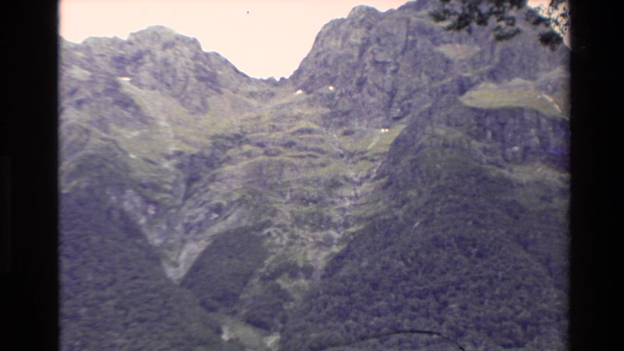 Rocky mountain face and green valley slopes framed by dark film edges.