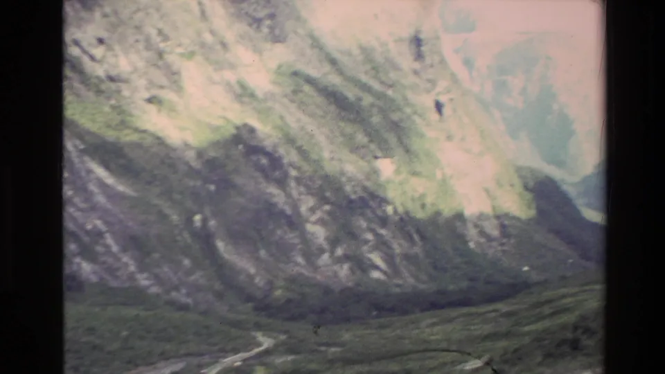 1982 New Zealand 8mm frame with a softer, motion-blurred view of pale rocky slopes, forested valley floor, and dark frame edges.