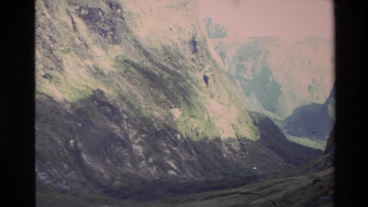 Steep green mountain walls and a shadowed valley seen through soft 8mm framing.