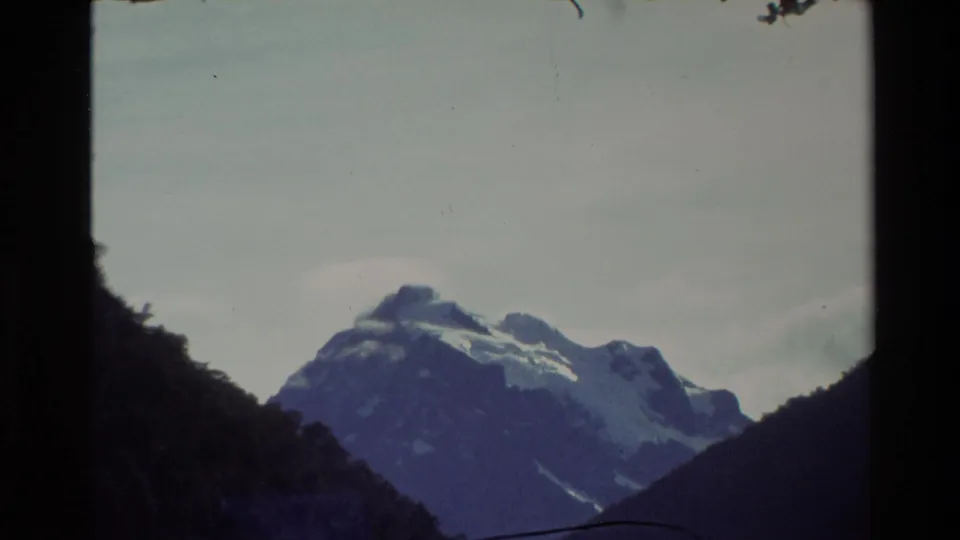 1982 New Zealand 8mm frame showing a distant snowy mountain partly framed by shadowed valley sides and soft, faded sky.