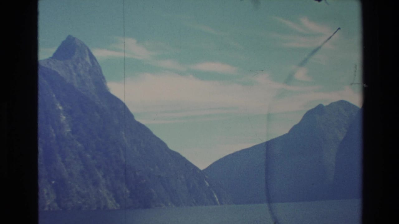 Mountain peak and adjoining dark slopes across a still lake with clouds overhead.