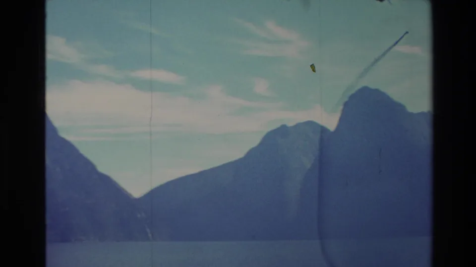 1982 New Zealand 8mm frame with distant slopes, a calm lake, pale clouds, and visible film wear from the scan.