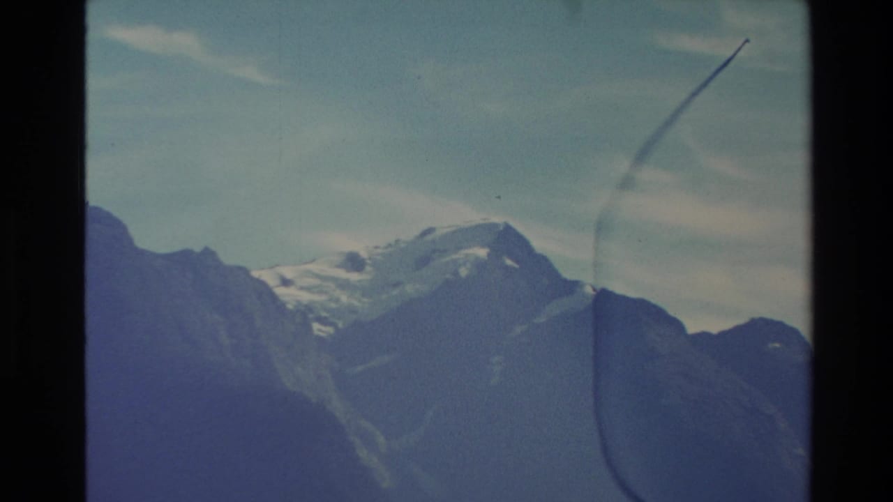 Snowy mountain peaks above dark alpine slopes under a pale blue sky.