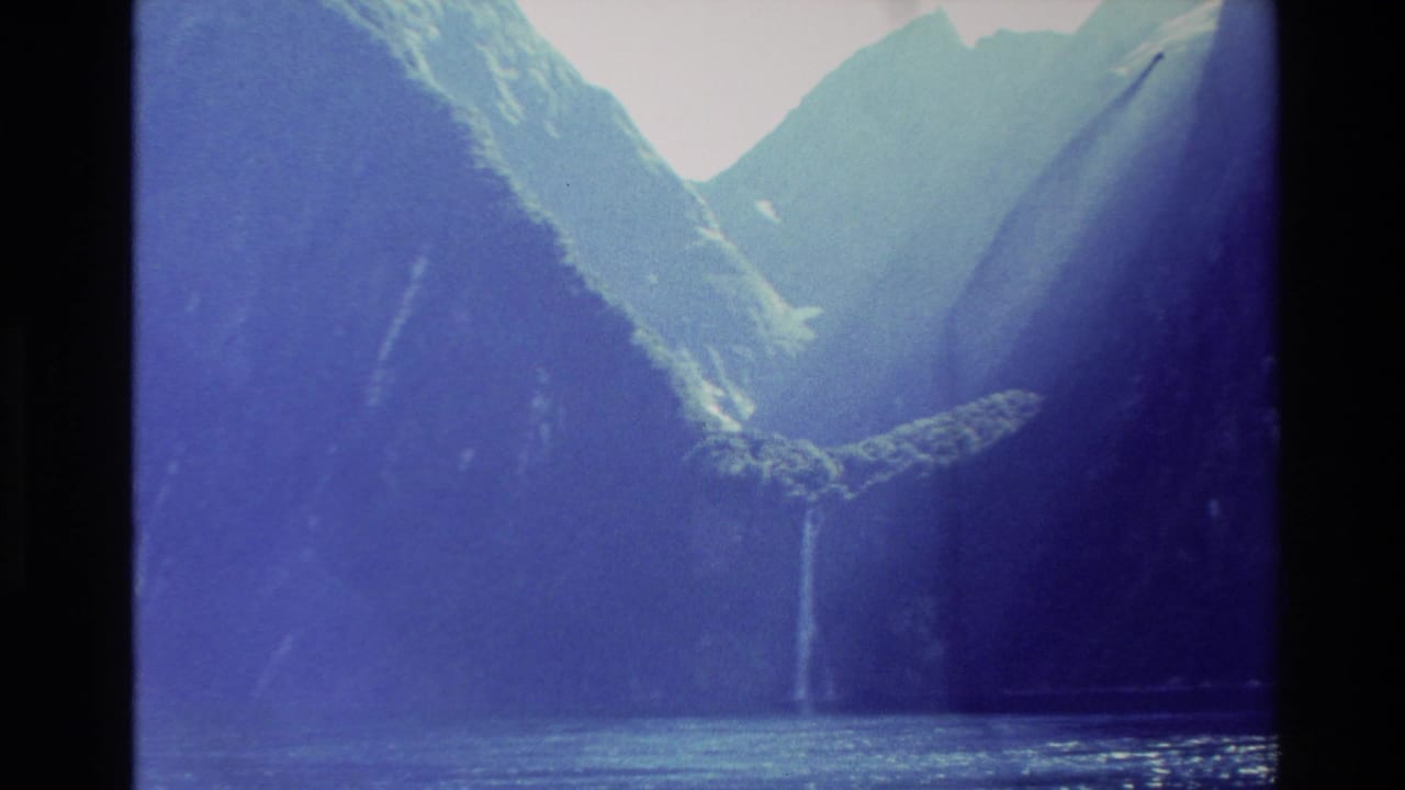 Mountain valley with steep walls, water, and a thin waterfall in the distance.