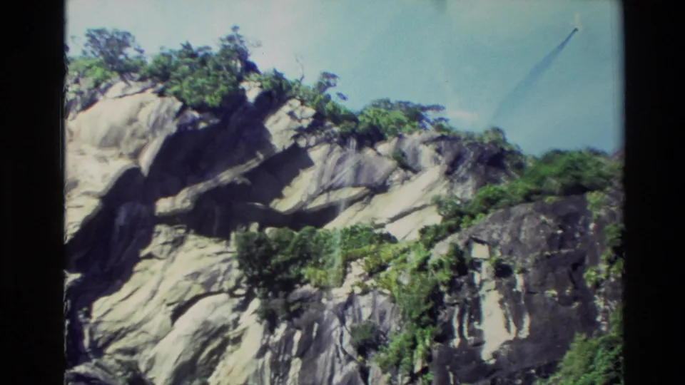 1982 New Zealand 8mm frame with pale, weathered cliff surfaces, dark crevices, and sparse greenery along the rocky coast.