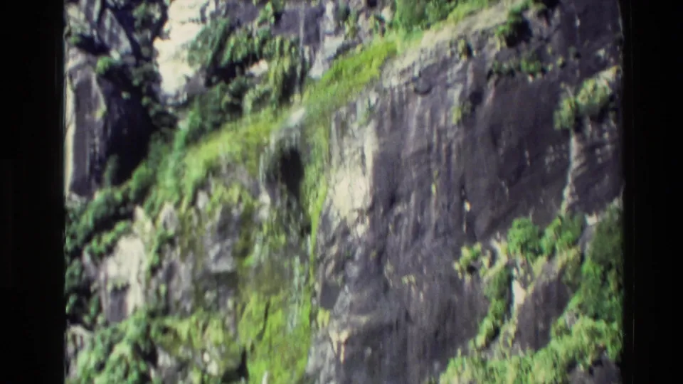 1982 New Zealand 8mm frame showing a darker cliff face with streaks of green vegetation as the boat moves past.