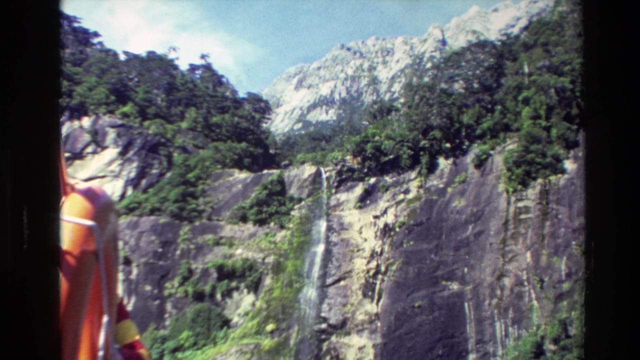 Rocky green mountainside with a waterfall seen from a boat window.