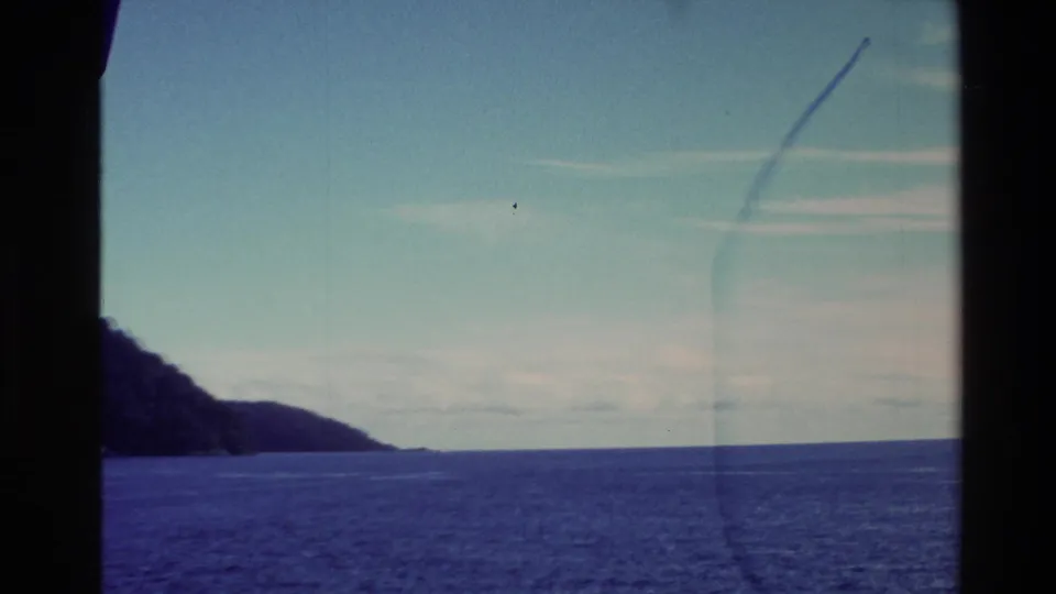 Open New Zealand water and a distant coastal headland appear under a pale sky in the final 1982 8mm travel frame.