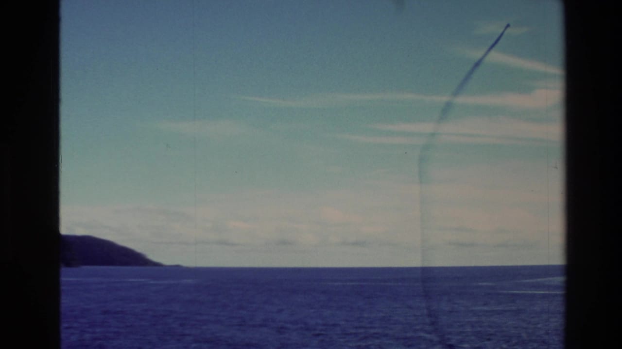 Wide ocean view with distant coastline, pale sky, and dark vertical frame edges.