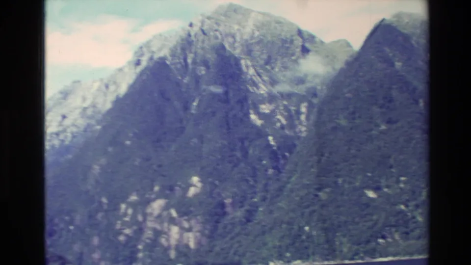 1982 New Zealand home-movie view of rugged mountain faces, green slopes, and scattered snow near the peaks.