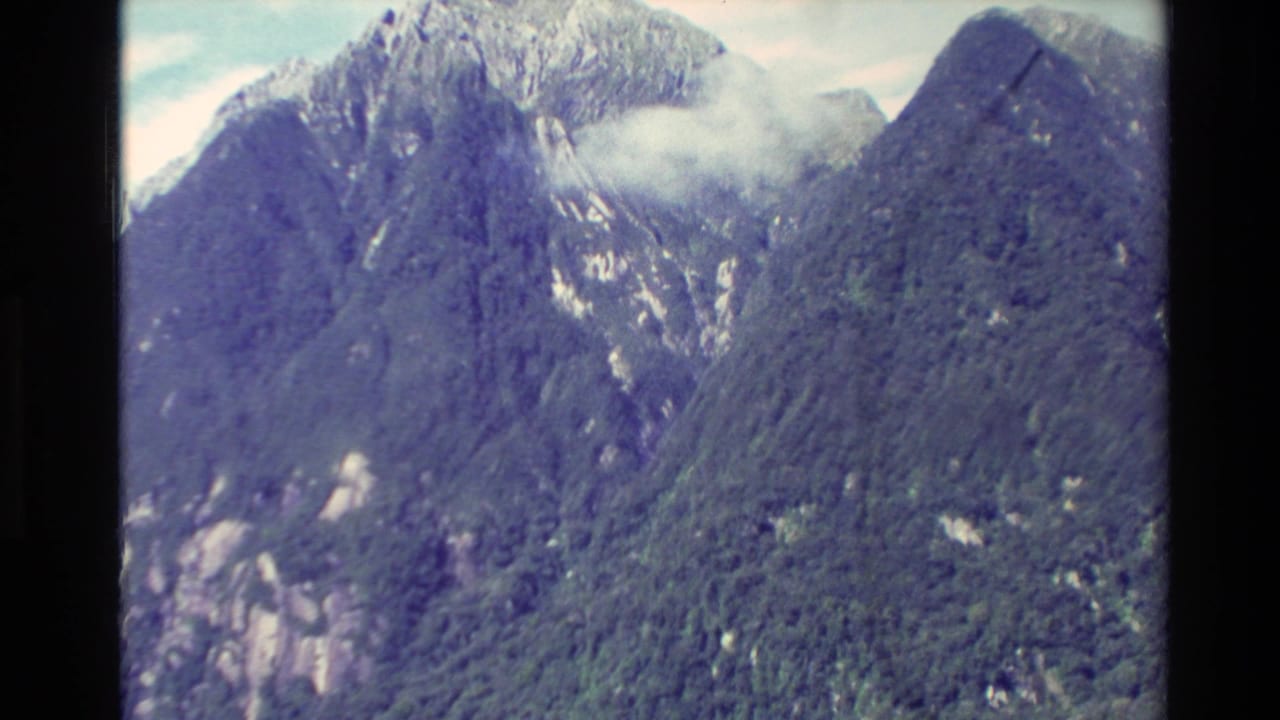 Forested mountain wall with rocky patches and cloud near the peak.