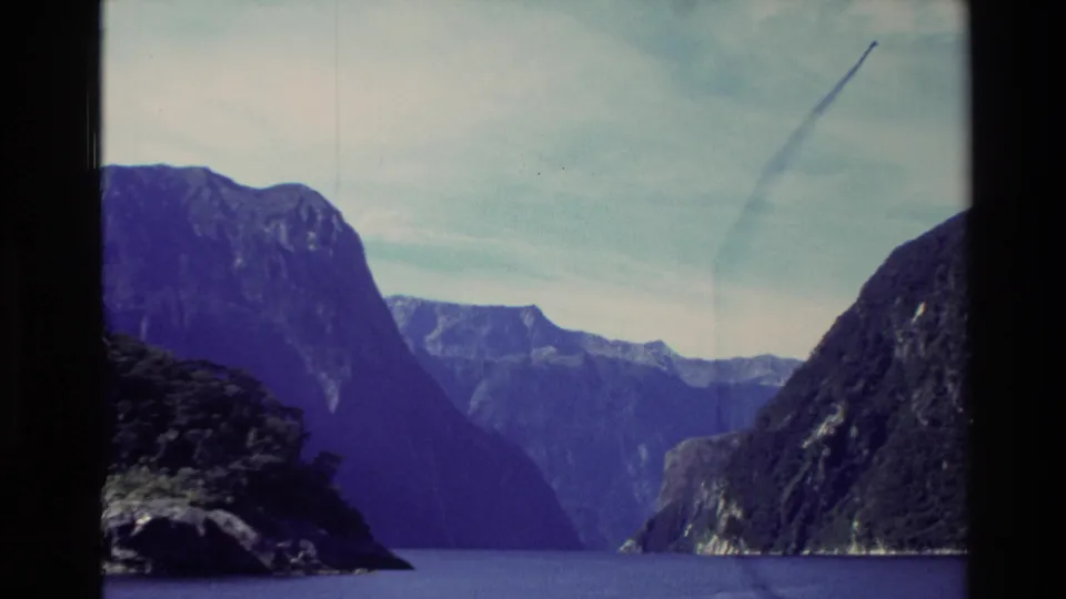1982 8mm New Zealand travel frame showing a tighter pan view across lake water and steep forested mountains.