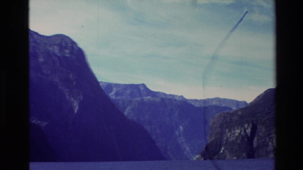 1982 New Zealand 8mm view of steep dark mountains above deep blue water during a ferry cruise.