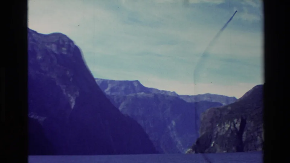 1982 New Zealand 8mm view of steep dark mountains above deep blue water during a ferry cruise.