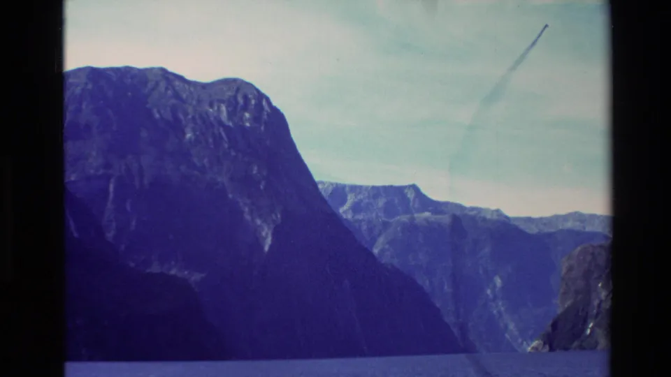 1982 New Zealand ferry view across rippling blue water toward steep mountains and distant ridges.
