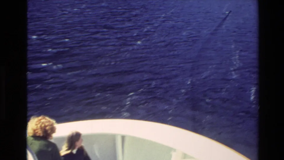 1982 New Zealand 8mm ferry-deck view with two tourists looking out across water toward mountains.