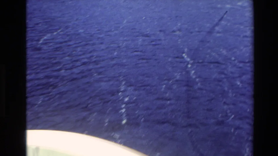 1982 New Zealand ferry-cruise frame focused on rippling blue water, wake lines, and distant mountain slopes.