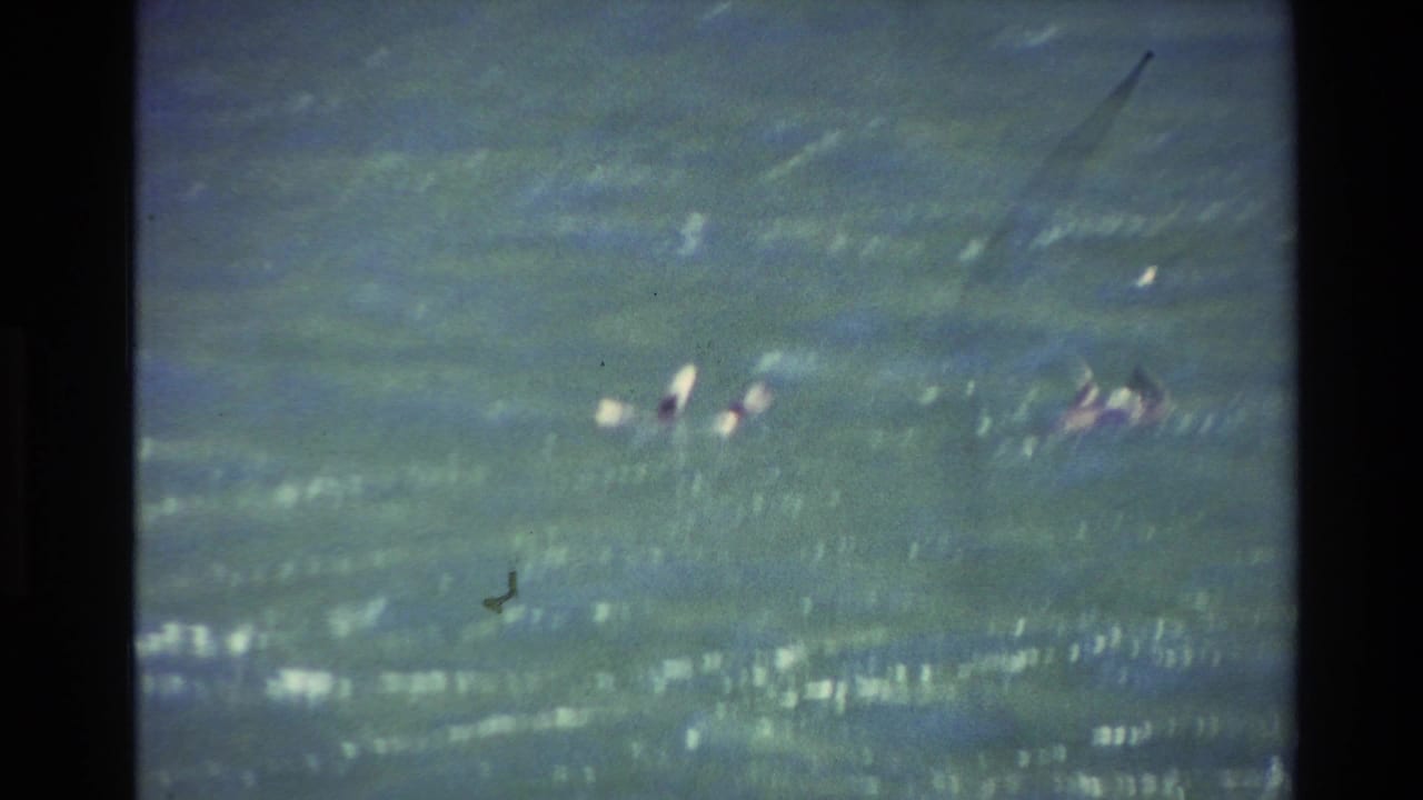 Small figures and pale surfboards are visible in rough green-blue water.